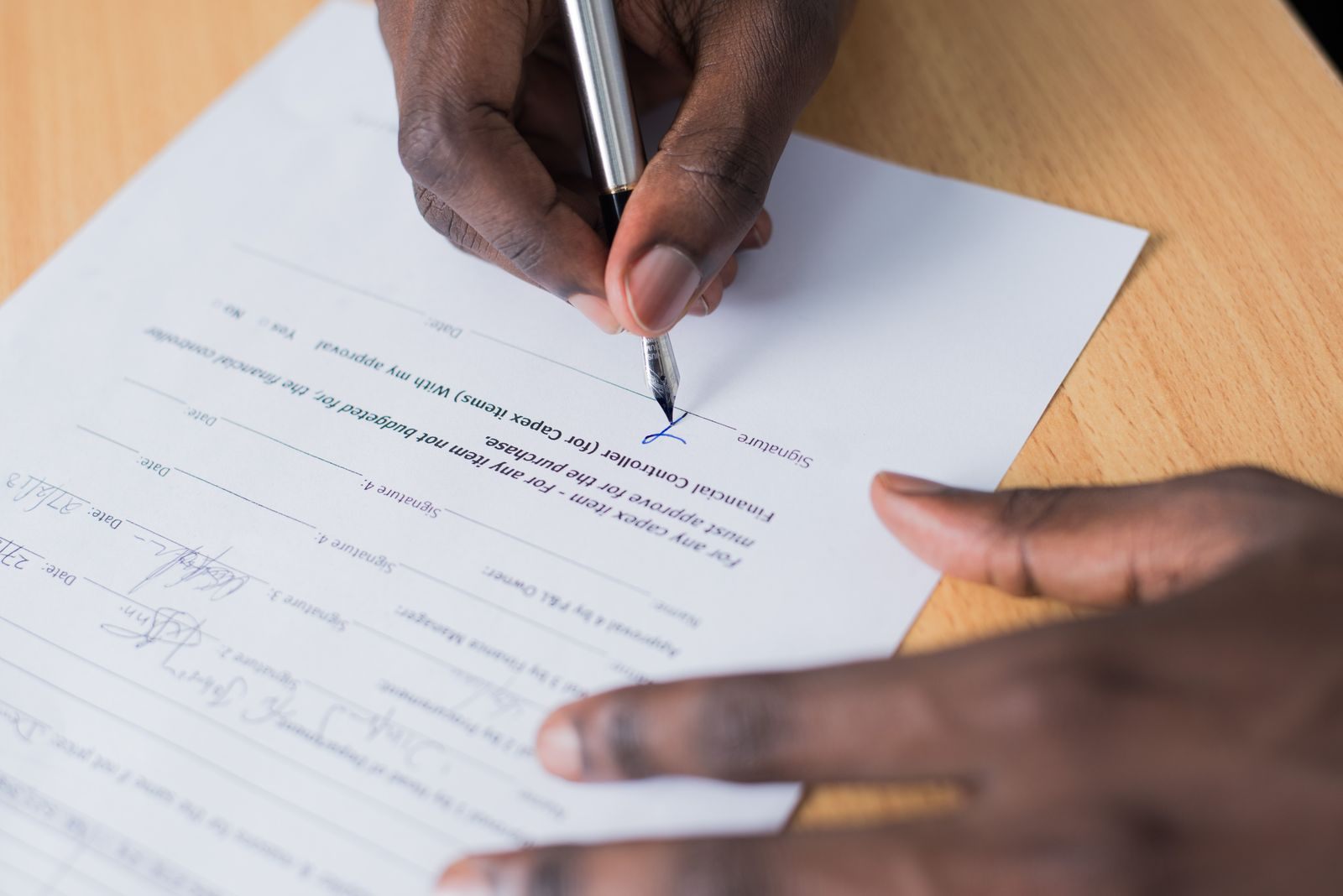 Hand signing an agreement on a wooden desk; signing on the spot is what a travel club membership scam relies on