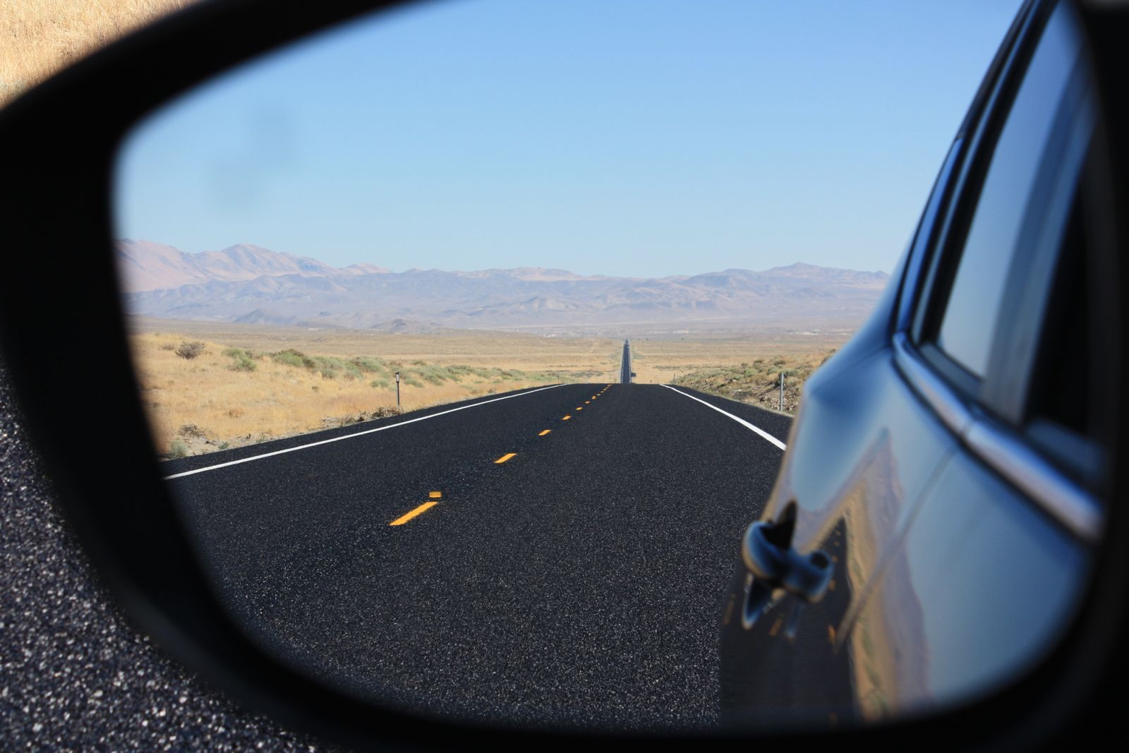 A straight desert highway reflected in a car side mirror under a blue sky
